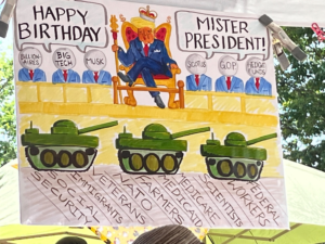 Poster displayed at the Denver No Kings Rally that shows Donald Trump watching a military parade with sycophants praising him while tanks run over Social Security and other essentials for the people.