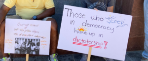 Two protest signs.  One says, "Get up, stand up for your rights before you don't have any" and the other says, "Those who sleep in democracy wake up in dictatorship"