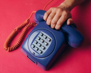 pexels-koolshooters-7346611 1 Image of hand on blue phone with red cord.