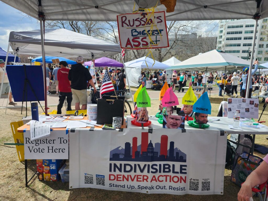 Image of Indivisible Denver Action table at the No Kings 3 rally.  The table features a ring toss game with caricatures of Trump cabinet members.