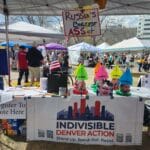 Image of Indivisible Denver Action table at the No Kings 3 rally. The table features a ring toss game with caricatures of Trump cabinet members.